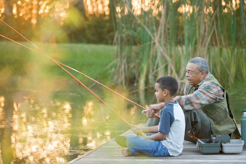 A grandfather and grandson go fishing at sunset.